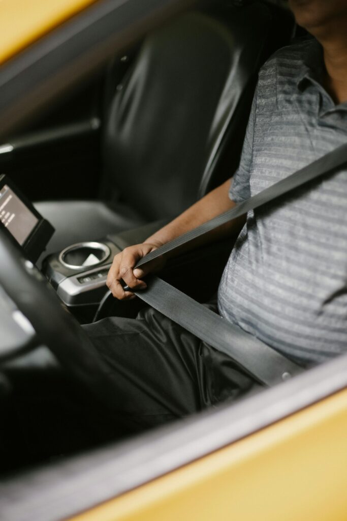 From above of crop unrecognizable male driver fastening seat belt while sitting in car in daytime